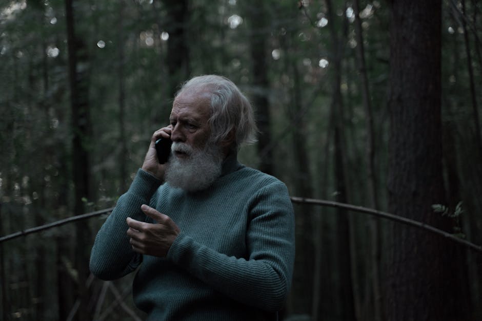 Senior man with grey hair using a smartphone in a serene forest.
