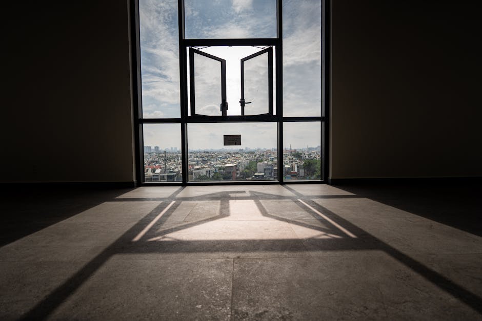 Sunlit room with open window framing a panoramic urban landscape view.